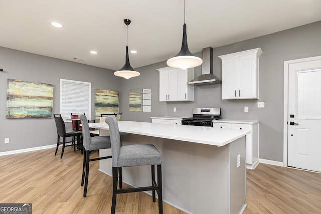 kitchen featuring pendant lighting, stainless steel stove, white cabinetry, a center island, and wall chimney exhaust hood