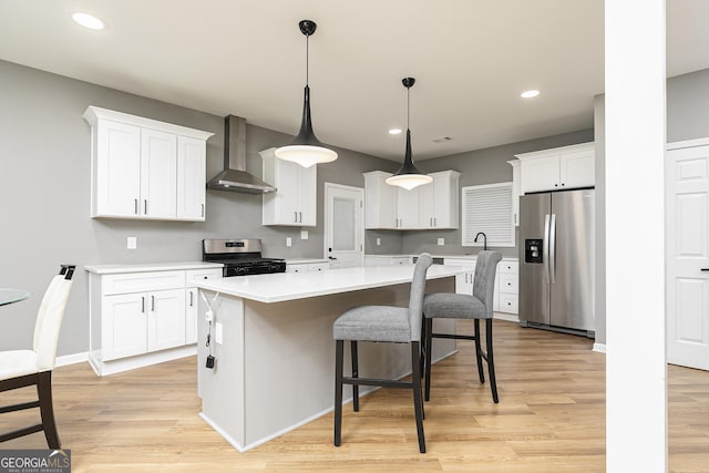 kitchen with wall chimney exhaust hood, a center island, hanging light fixtures, appliances with stainless steel finishes, and white cabinets