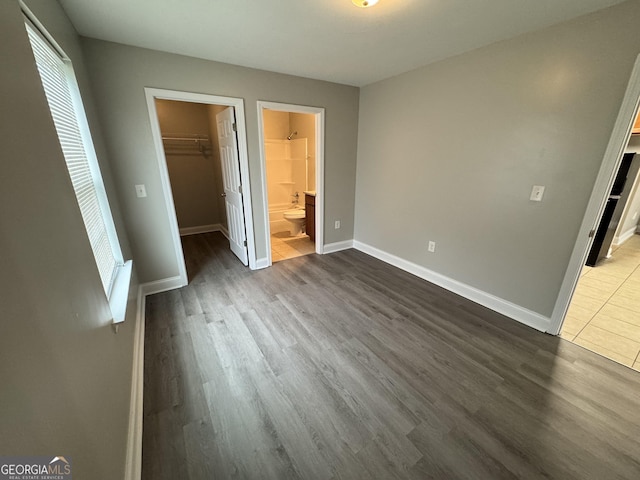 unfurnished bedroom featuring a spacious closet, a closet, ensuite bathroom, and dark wood-type flooring