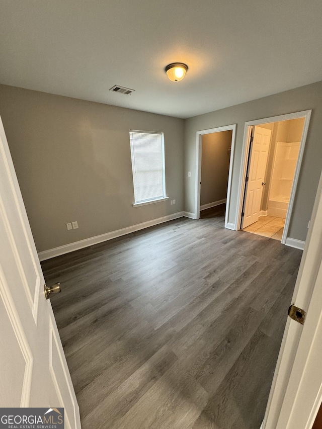 unfurnished bedroom featuring ensuite bathroom and dark hardwood / wood-style flooring