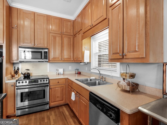 kitchen featuring appliances with stainless steel finishes, crown molding, hardwood / wood-style floors, and sink