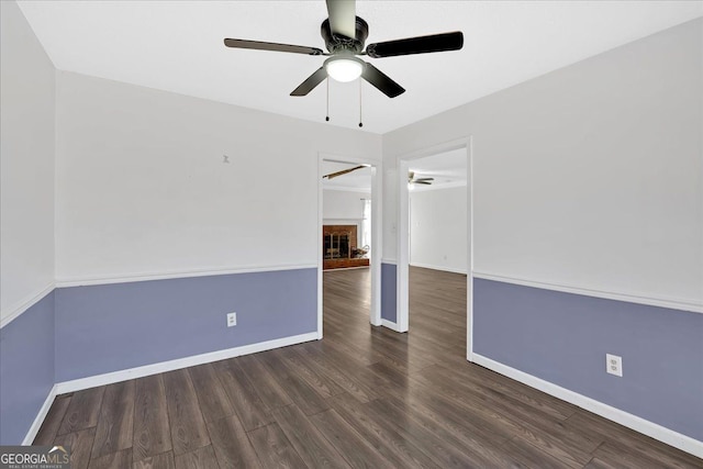 unfurnished room featuring ceiling fan, dark wood-type flooring, and a fireplace