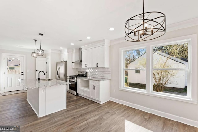 kitchen with sink, appliances with stainless steel finishes, a kitchen island with sink, white cabinets, and decorative light fixtures