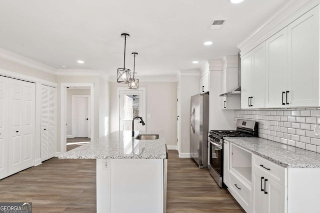 kitchen featuring appliances with stainless steel finishes, an island with sink, sink, white cabinets, and hanging light fixtures