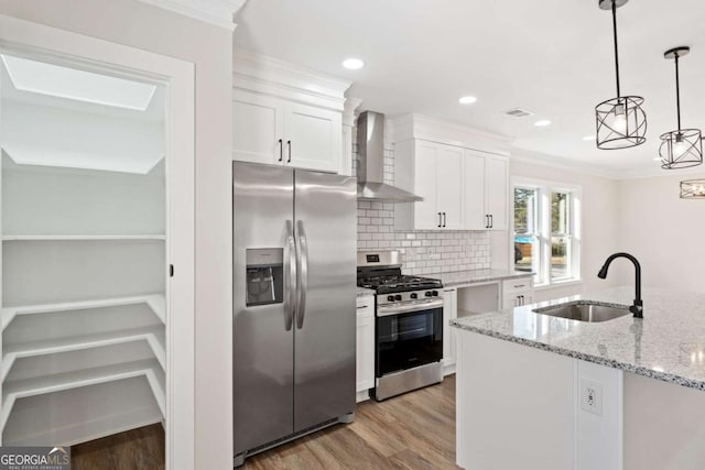 kitchen with wall chimney range hood, sink, appliances with stainless steel finishes, white cabinetry, and hanging light fixtures