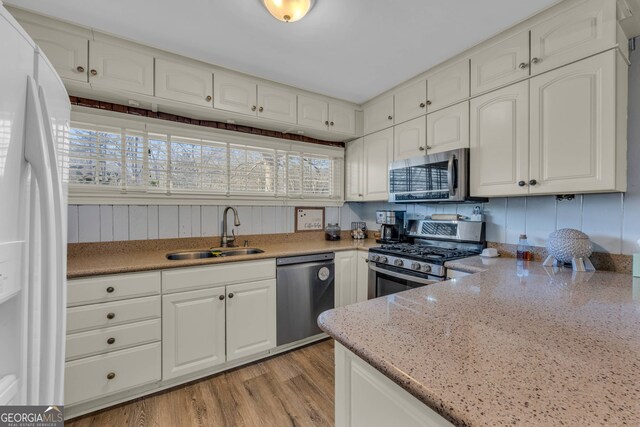 kitchen featuring light hardwood / wood-style flooring, appliances with stainless steel finishes, light stone countertops, white cabinets, and decorative backsplash