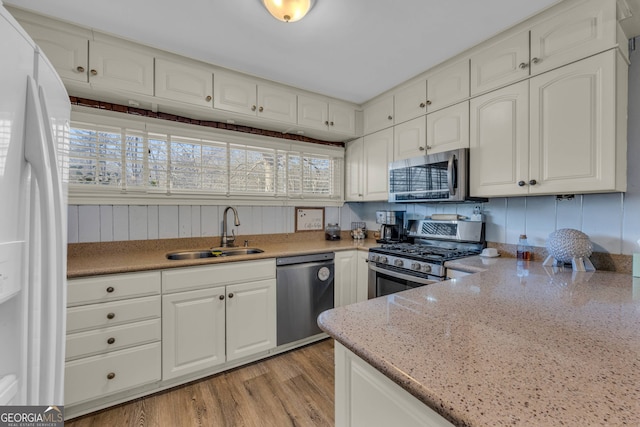 kitchen featuring light stone countertops, light wood finished floors, a sink, stainless steel appliances, and white cabinetry