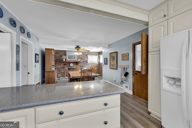 kitchen featuring brick wall, light stone countertops, white refrigerator with ice dispenser, and white cabinets