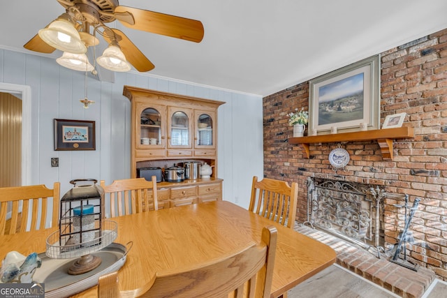 dining space featuring ornamental molding, wooden walls, ceiling fan, a fireplace, and light hardwood / wood-style floors