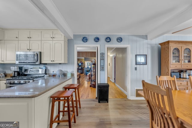 kitchen with light hardwood / wood-style flooring, appliances with stainless steel finishes, white cabinetry, light stone counters, and ornamental molding