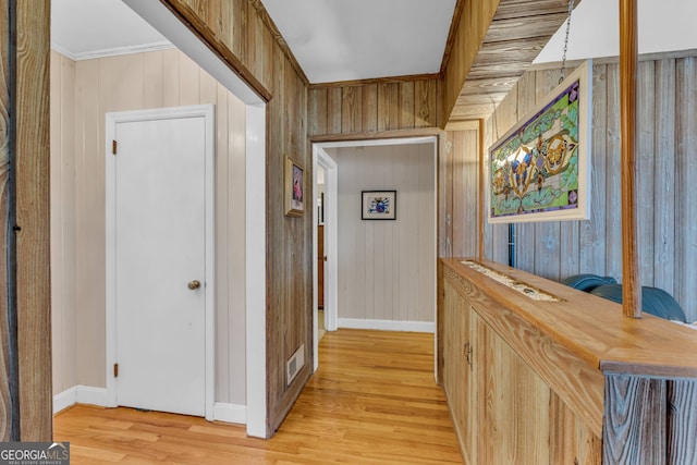 hallway featuring visible vents, baseboards, wood walls, ornamental molding, and light wood-style floors