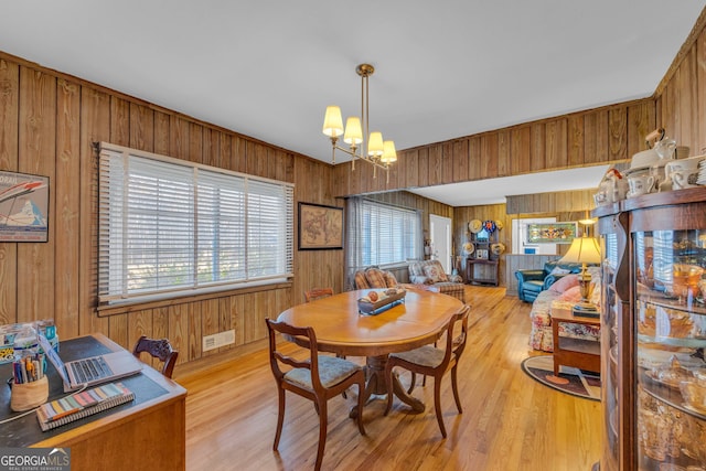 dining space featuring an inviting chandelier, light hardwood / wood-style flooring, and wood walls