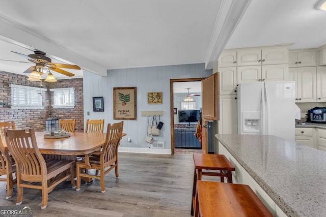 dining space with beamed ceiling, ceiling fan, brick wall, and light hardwood / wood-style floors