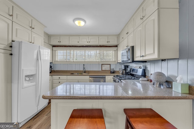 kitchen featuring sink, a breakfast bar, appliances with stainless steel finishes, white cabinets, and kitchen peninsula