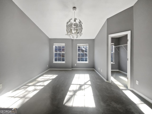 unfurnished bedroom with a closet, an inviting chandelier, dark colored carpet, and lofted ceiling