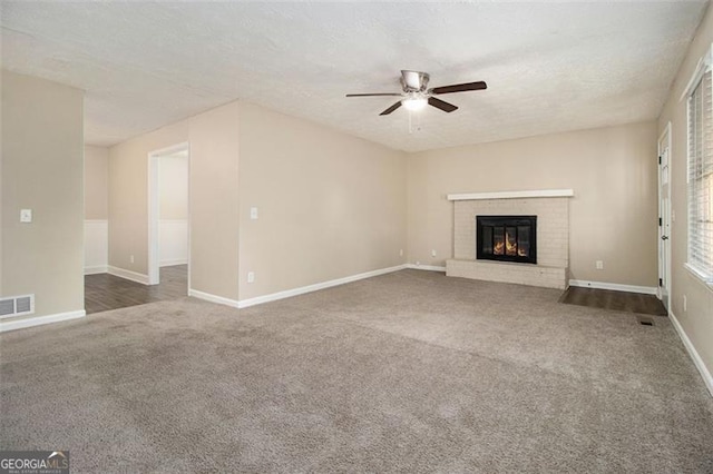 unfurnished living room featuring a textured ceiling, a brick fireplace, dark carpet, and ceiling fan