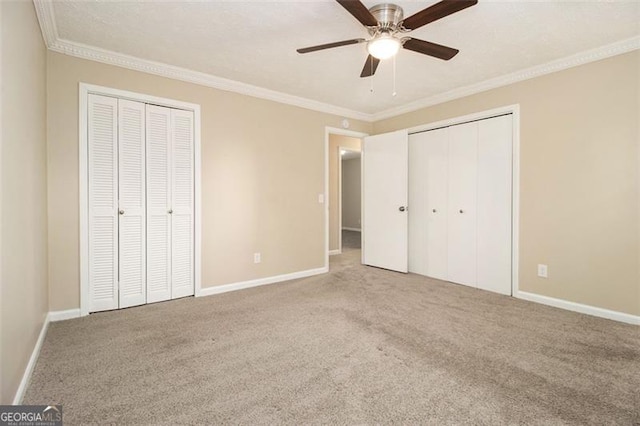 unfurnished bedroom with ceiling fan, two closets, crown molding, and carpet flooring