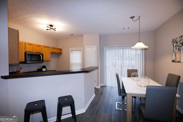 kitchen featuring baseboards, brown cabinets, stainless steel microwave, dark countertops, and dark wood finished floors