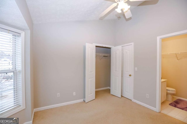 unfurnished bedroom featuring ceiling fan, a textured ceiling, ensuite bathroom, and light carpet