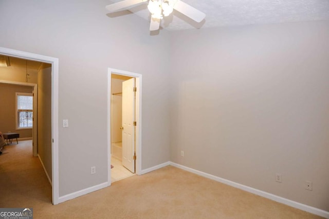 unfurnished bedroom featuring ceiling fan, light colored carpet, a textured ceiling, and ensuite bath