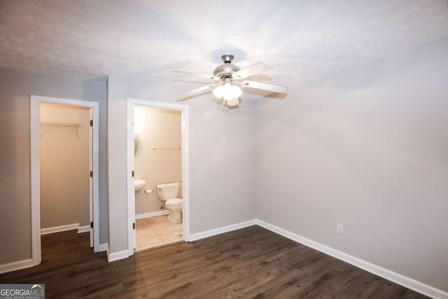 unfurnished bedroom featuring ceiling fan, connected bathroom, a walk in closet, a closet, and dark hardwood / wood-style flooring