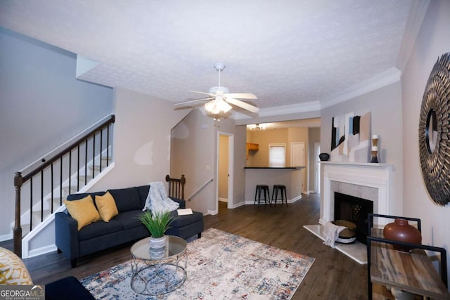 living area with a textured ceiling, a premium fireplace, wood finished floors, baseboards, and stairs