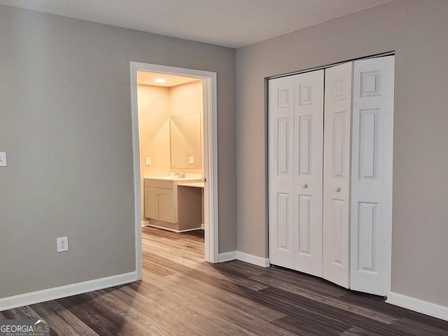 unfurnished bedroom with a closet, ensuite bathroom, and dark hardwood / wood-style floors