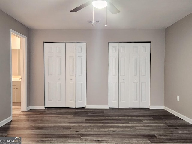 unfurnished bedroom with ceiling fan, dark hardwood / wood-style flooring, and two closets