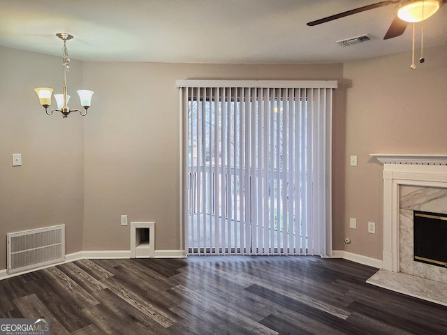 unfurnished living room featuring ceiling fan with notable chandelier, dark wood-type flooring, and a premium fireplace