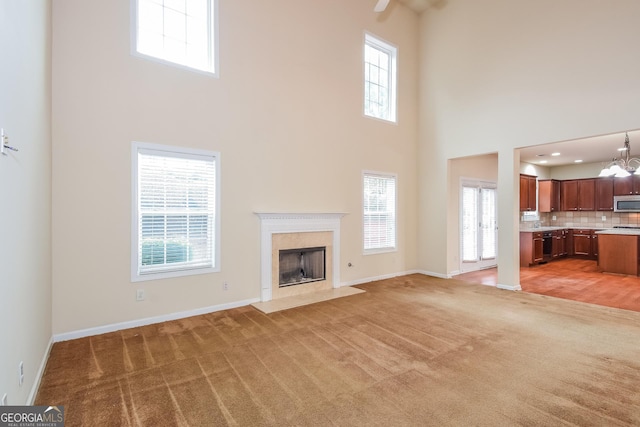 unfurnished living room featuring carpet, an inviting chandelier, a premium fireplace, and a high ceiling