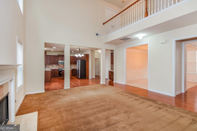 unfurnished living room featuring a high ceiling, light colored carpet, a high end fireplace, and a notable chandelier