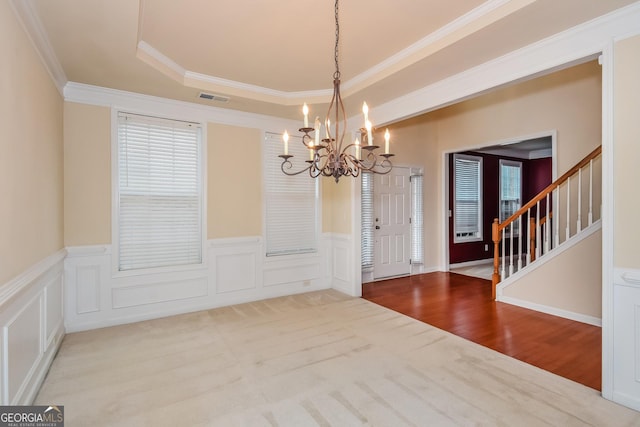 unfurnished dining area with a notable chandelier, a tray ceiling, ornamental molding, and hardwood / wood-style flooring