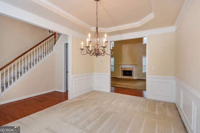 unfurnished dining area featuring a raised ceiling, ornamental molding, a chandelier, and carpet flooring