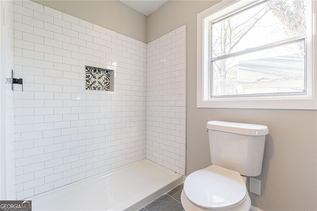 bathroom featuring toilet, tile patterned flooring, and a tile shower