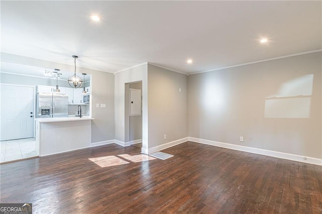 unfurnished living room with ornamental molding, sink, a chandelier, and dark hardwood / wood-style floors