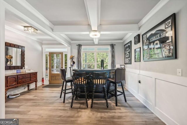 dining area featuring beam ceiling, bar area, crown molding, and light hardwood / wood-style floors