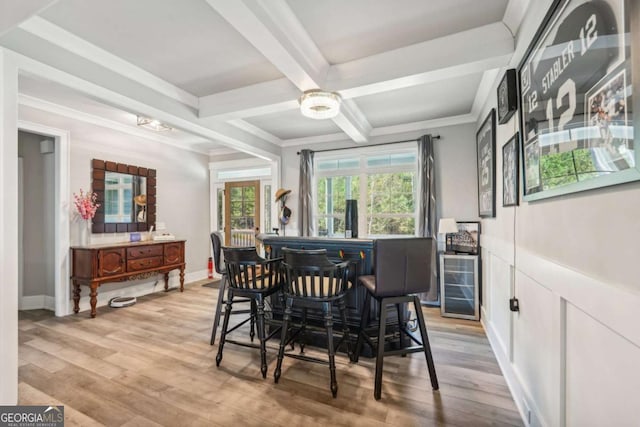 dining area featuring light hardwood / wood-style floors, coffered ceiling, ornamental molding, indoor bar, and beam ceiling