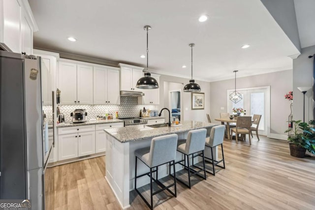 kitchen with hanging light fixtures, white cabinets, an island with sink, and stainless steel appliances