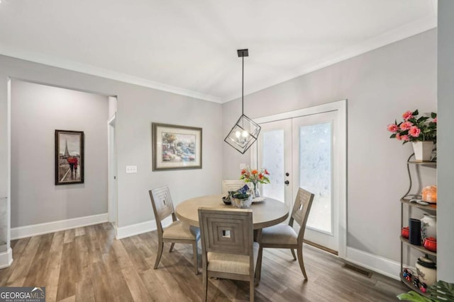 dining space with wood-type flooring, ornamental molding, french doors, and an inviting chandelier