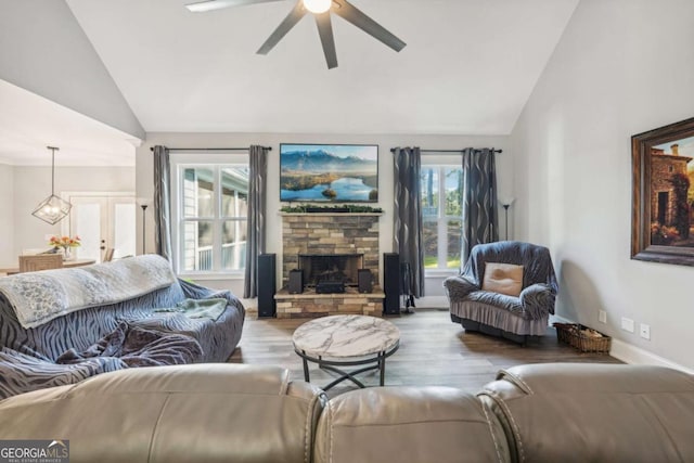 living room featuring vaulted ceiling, a stone fireplace, light wood-type flooring, and ceiling fan