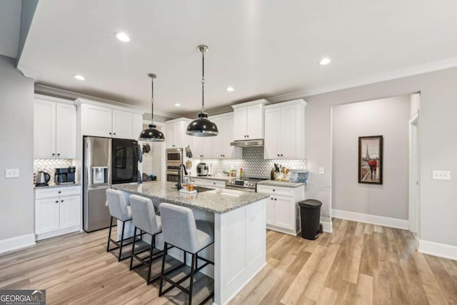 kitchen with a center island with sink, light stone countertops, stainless steel appliances, and white cabinetry