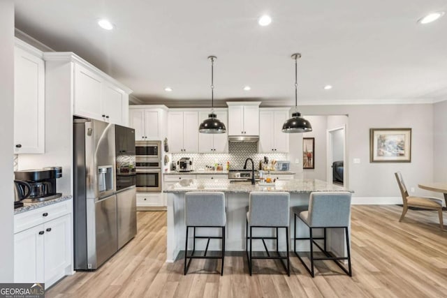 kitchen featuring pendant lighting, white cabinets, stainless steel appliances, a kitchen island with sink, and light stone counters