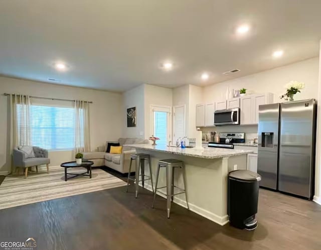 kitchen featuring white cabinetry, stainless steel appliances, an island with sink, light stone counters, and a breakfast bar