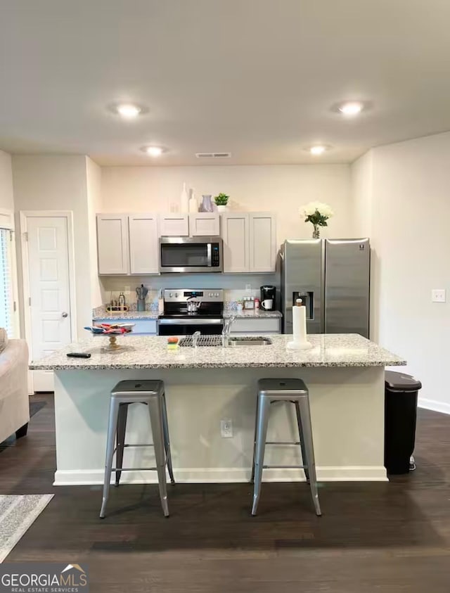 kitchen with white cabinetry, appliances with stainless steel finishes, a center island with sink, and a breakfast bar area