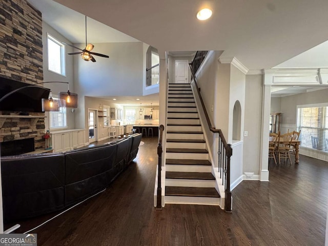 stairs with ceiling fan, crown molding, wood-type flooring, and a stone fireplace