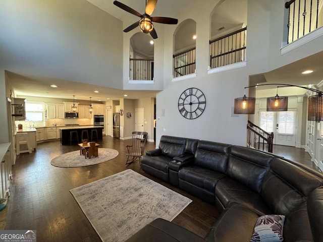 living room with ceiling fan, a high ceiling, and dark hardwood / wood-style floors