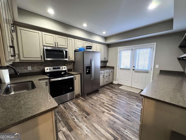 kitchen featuring stainless steel appliances, decorative backsplash, dark hardwood / wood-style floors, dark stone countertops, and sink