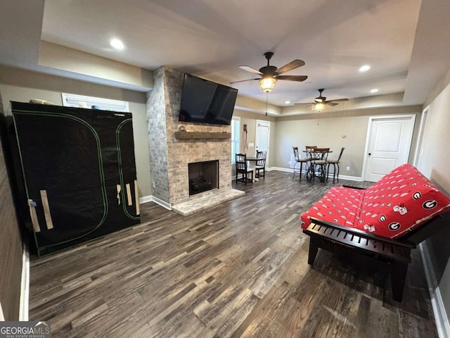 living room with a tray ceiling, hardwood / wood-style floors, and a stone fireplace