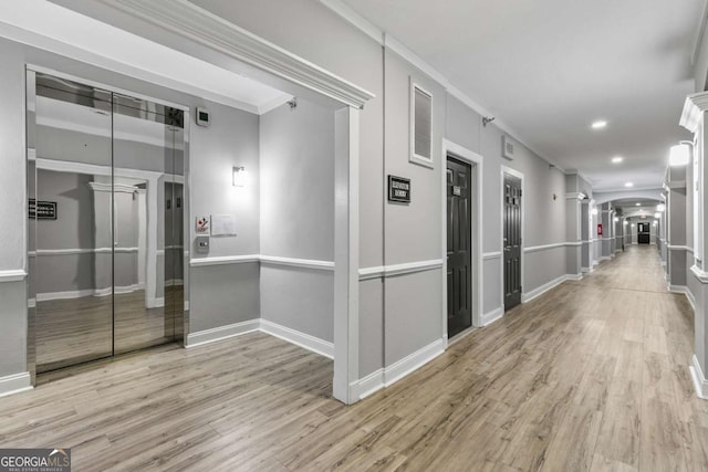 corridor with light wood-type flooring, crown molding, and decorative columns