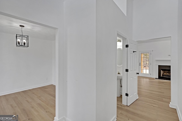 hall with a towering ceiling, a chandelier, and light hardwood / wood-style floors